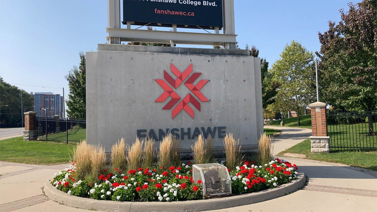 An exterior sign that has the Fanshawe logo on it, with flowers in front.