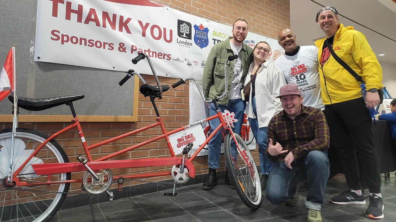 Five people posing with a red bike in front of a banner thanking sponsors.
