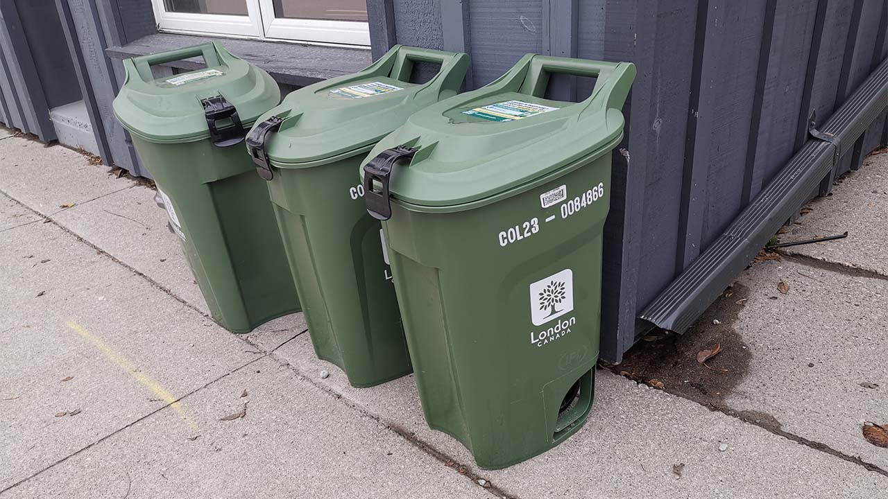 A photo of three green bins on a city curb.