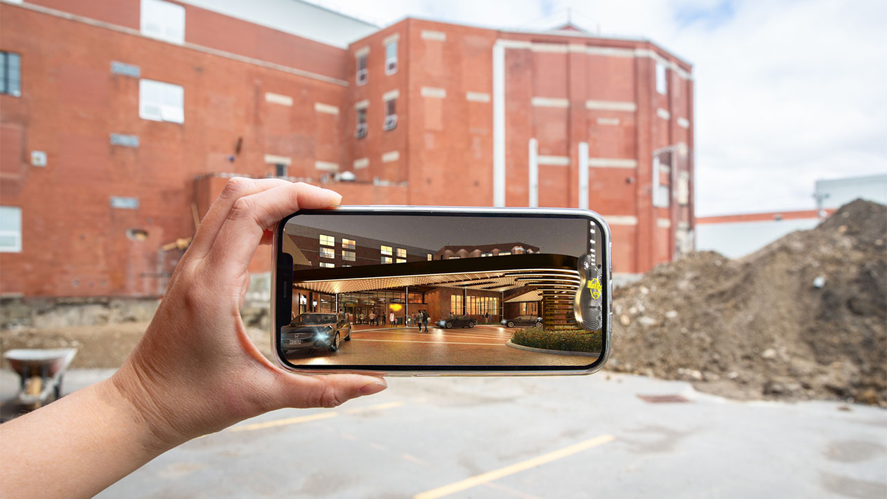 Photo of a picture of the new Hard Rock Hotel on a phone, held up in front of the current 100 Kellogg Lane building.