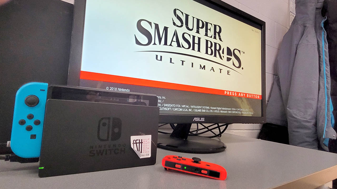 A Nintendo Switch in front of a monitor showing the Super Smash Bros. logo