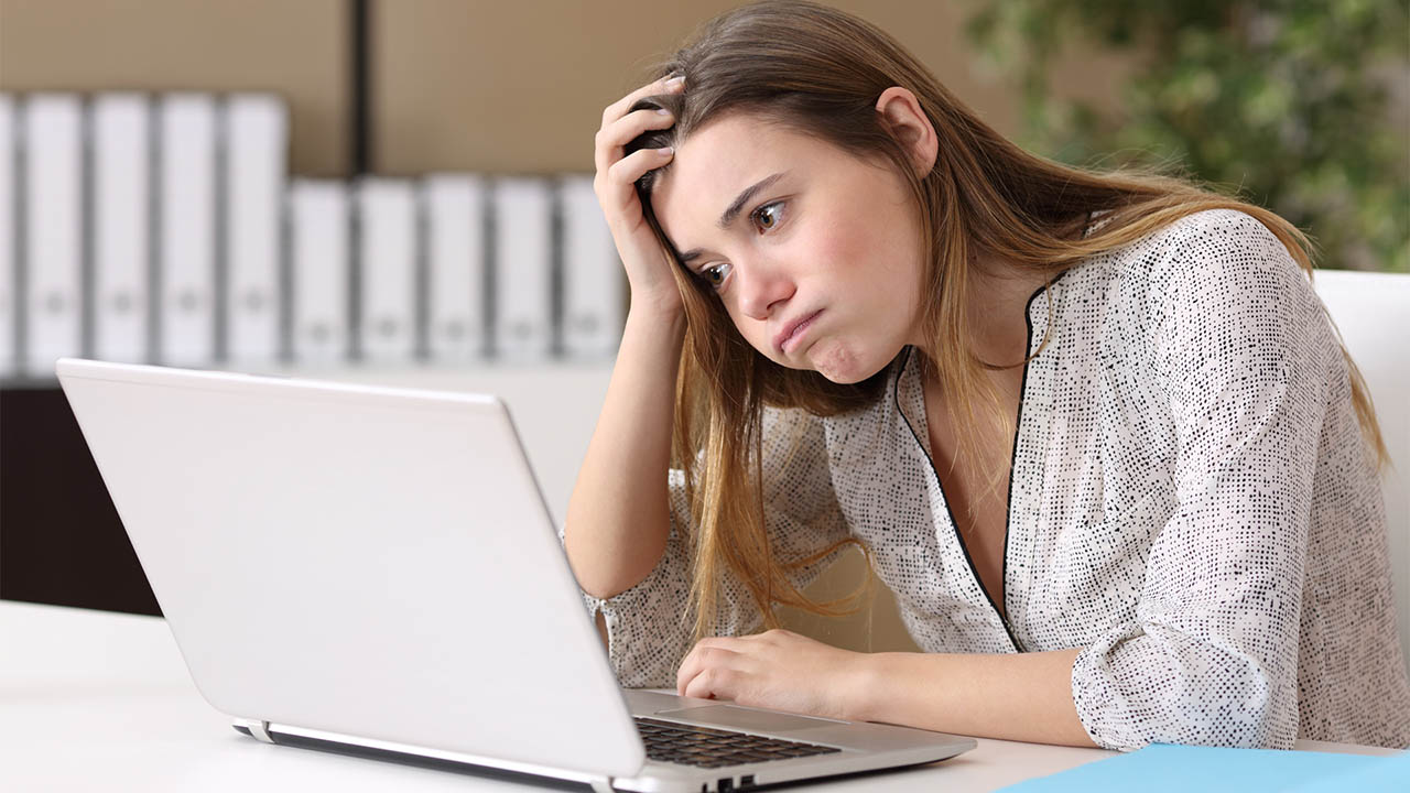 A young woman appears saddened behind a computer screen.