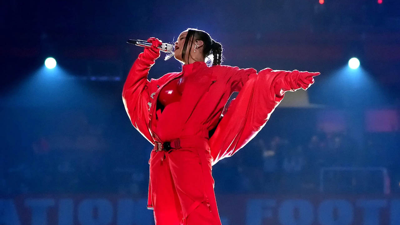 Rihanna singing into a microphone, wearing a red outfit.