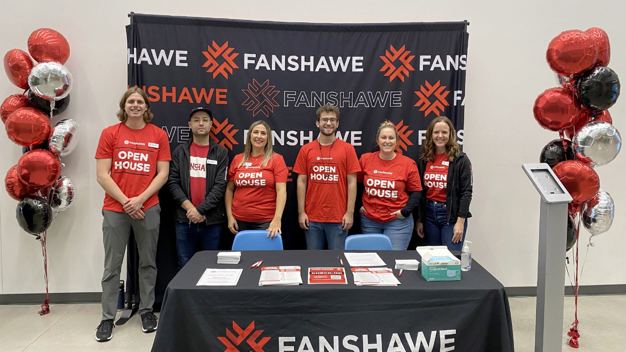 Photo of a group of volunteers standing behind a desk, all wearing Fanshawe-branded attire.