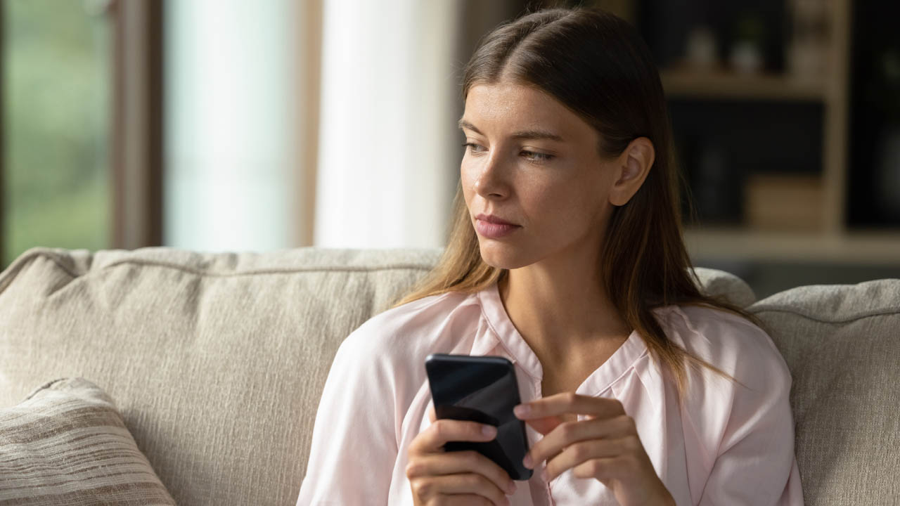 Stock photo of a woman holding a cell phone, with an unsure expression on her face