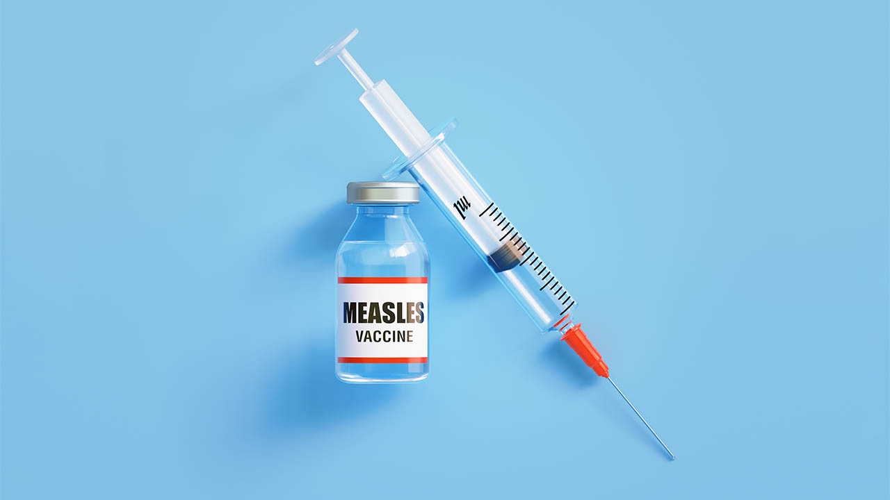 Stock image of a gloved hand preparing a measles vaccination shot.