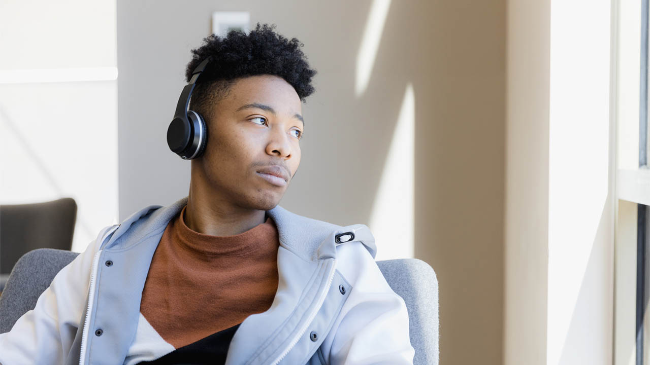 A photo of a young man wearing headphones, looking sadly out of a window.