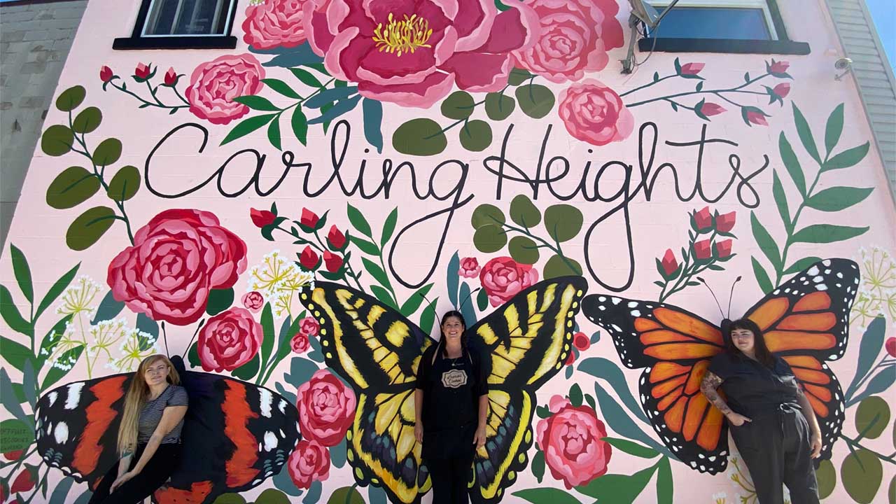 Pamela Scharback, Laurie Butterworth, and Alana Hryclik stand in front of the Carling Heights mural.