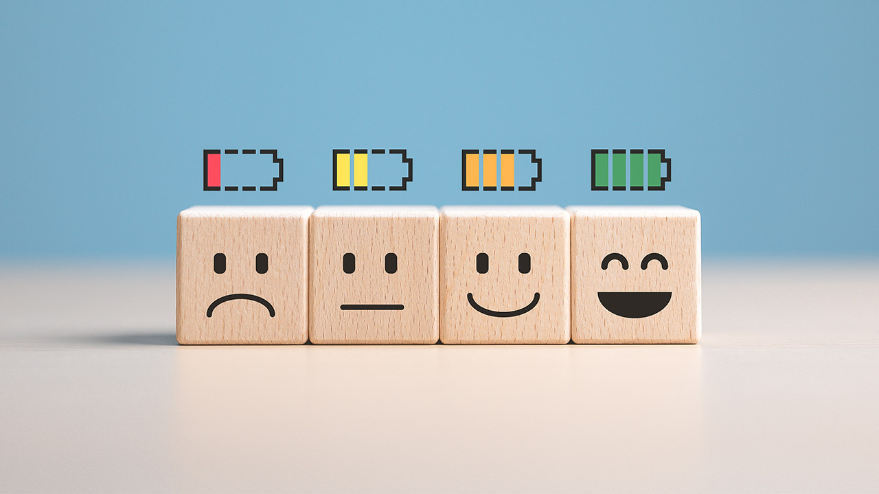 A stock image of wooden blocks with faces on them, showing emotions from sad to happy, with battery levels above them. The highest battery level is above the block with the happiest expression. 