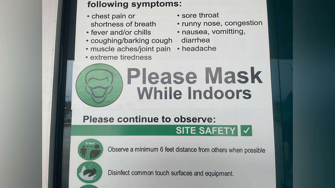 A sign asking people to please wear a mask while indoors along with symptoms to watch out for.