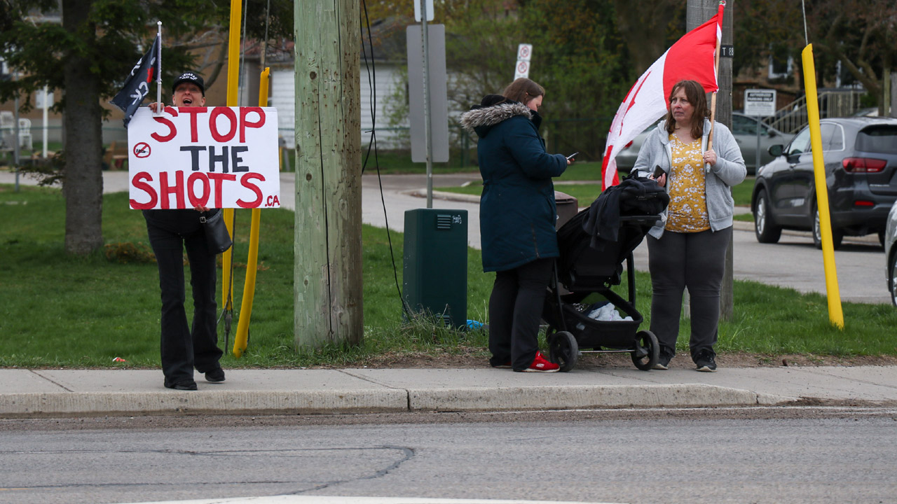 A group of protesters with a sign that says Stop the Shot.